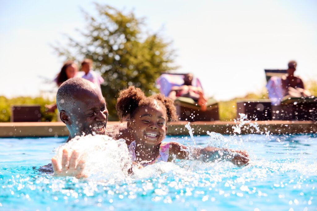 Grandfather Teaching Granddaughter To Swim In Outdoor Pool On Ho